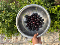 Steel ki chalni me taaza kaale-baingani jamun fruits, haath me pakde hue