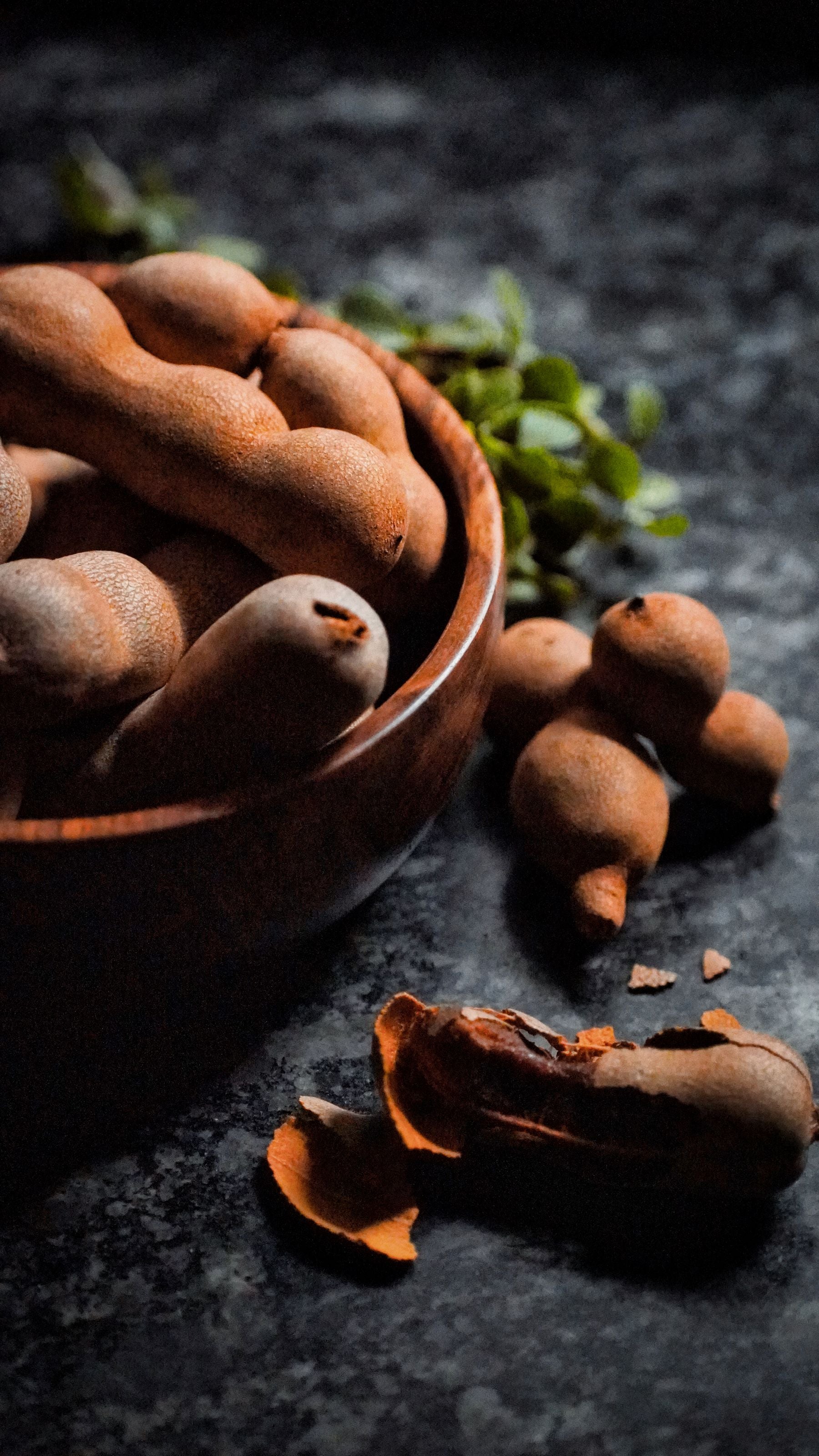 Imli ke pods (tamarind) ek lakdi ke bowl me, ek pod khula hua jisme andar ka gooda dikh raha hai